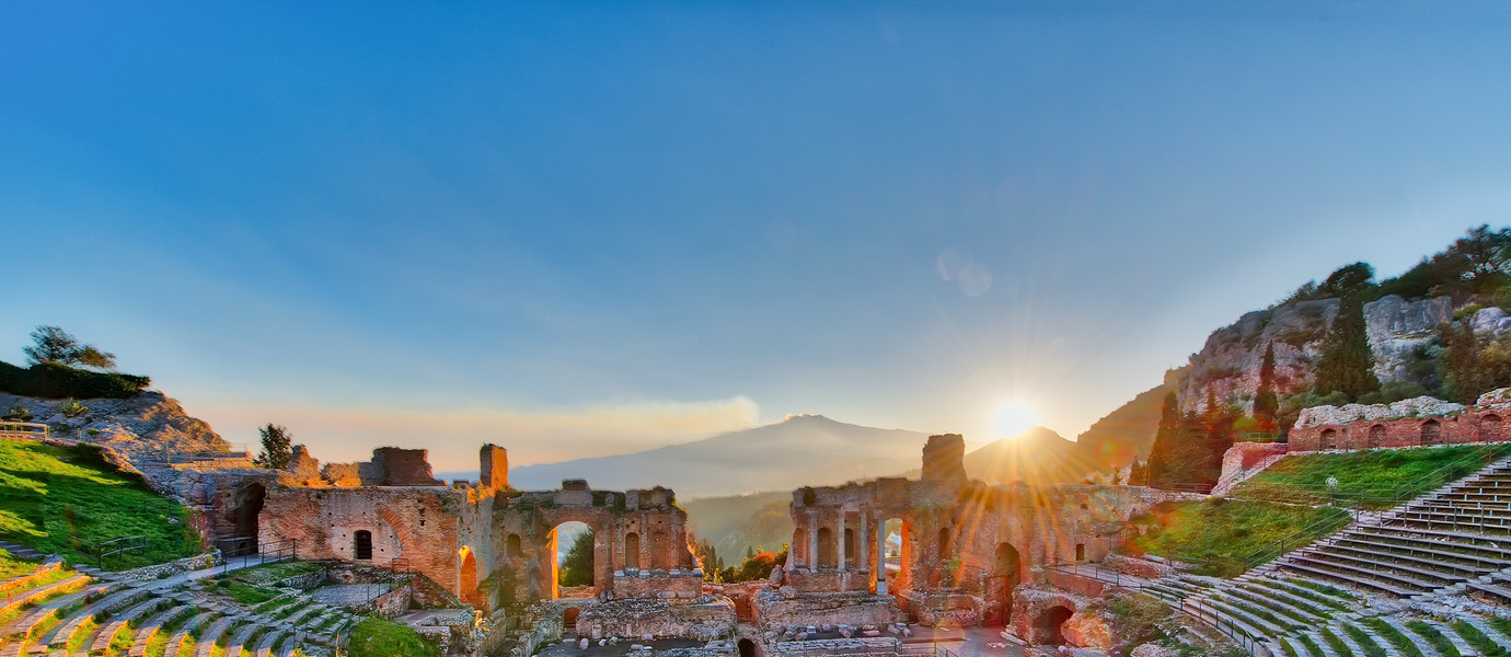 Ancient theatre of Taormina Siciliy Italy  with Etna erupting volcano at sunset